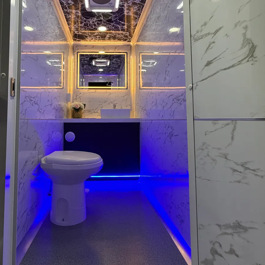 Inside one of the restrooms: a flush toilet, a vanity with a vessel sink and a backlit mirror, marble-effect walls and blue floor lighting